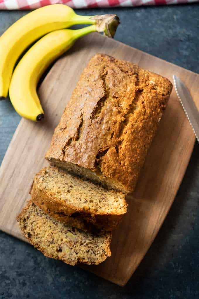 Banana bread with a couple slices cut on a cutting board next to two bananas