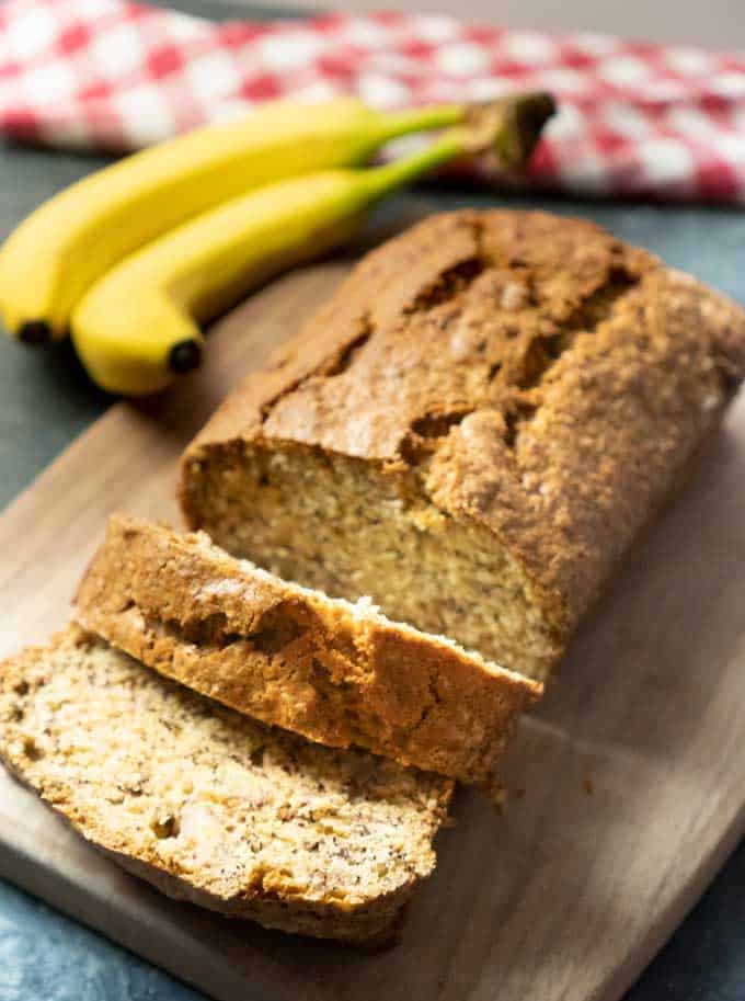 Banana bread with a couple slices cut on a cutting board next to two bananas