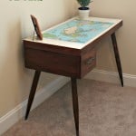 A wooden desk with a map table top with a picture frame and small pant on it