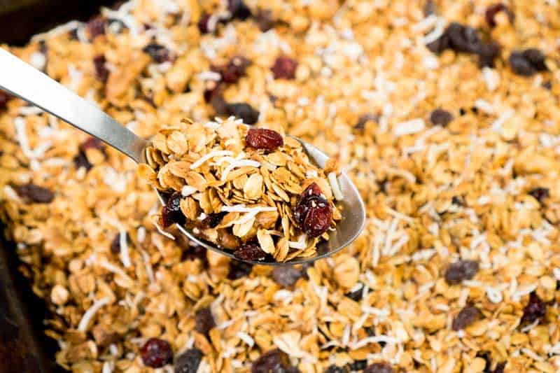 best homemade granola with raisins and dried cranberries in spoon held over baking sheet