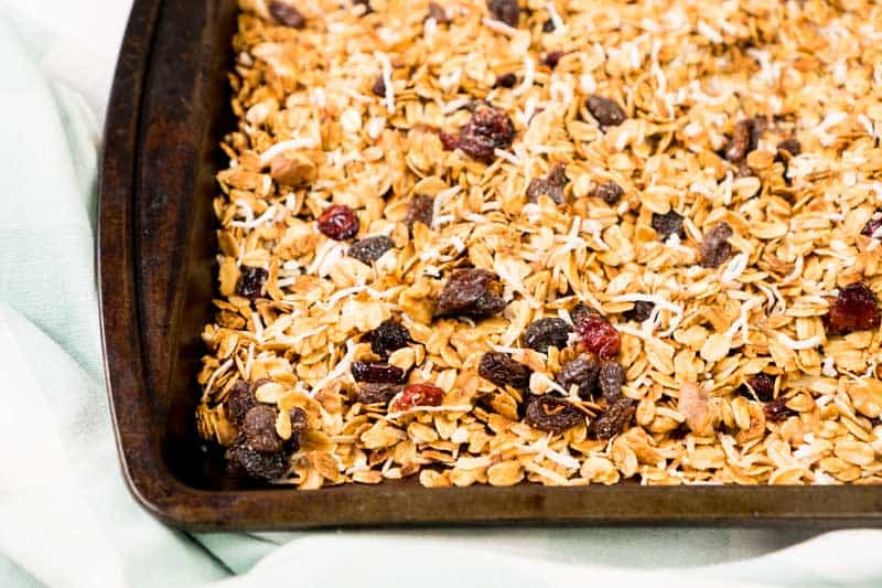 close up photo of homemade granola with raisins and dried cranberries on baking sheet