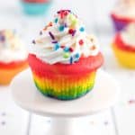 rainbow colored cupcake topped with vanilla frosting and sprinkles