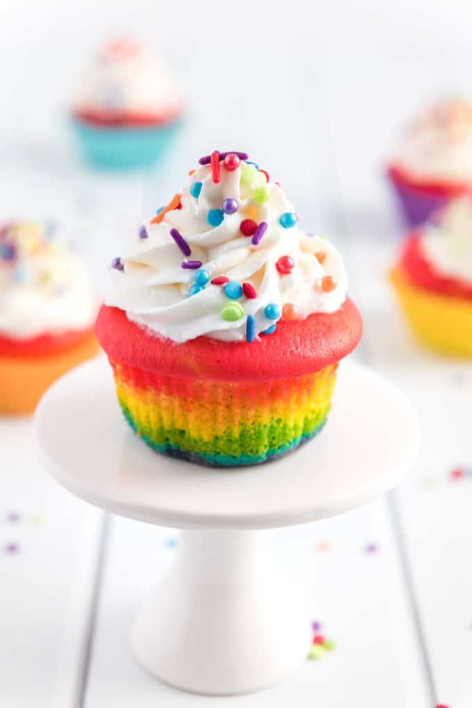 rainbow colored cupcake topped with vanilla frosting and sprinkles