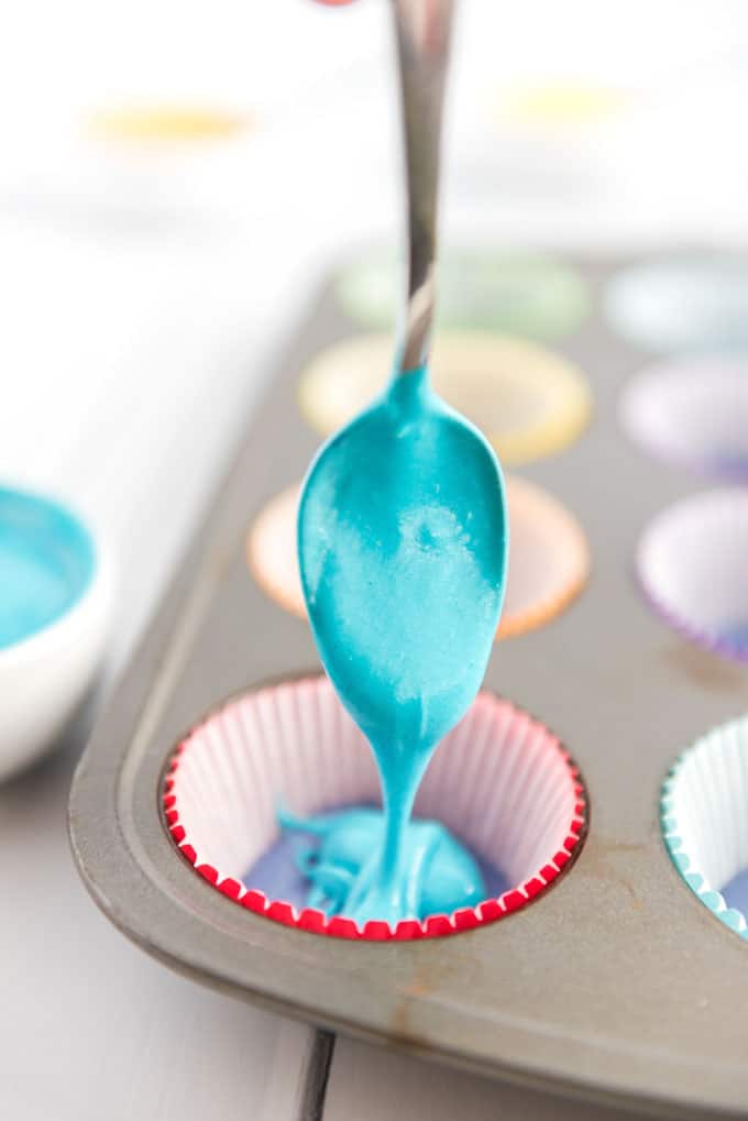 adding blue batter to rainbow cupcakes in muffin pan