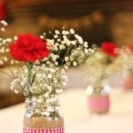 A close up of rustic bridal shower table centerpieces including baby's breath and red carnations