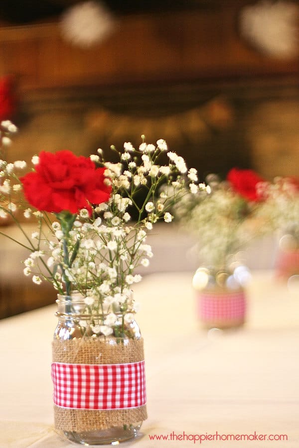 A close up of rustic bridal shower table centerpieces including baby's breath and red carnations 