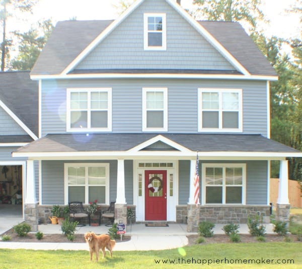 blue craftsman three story home with red door and dog in front yard