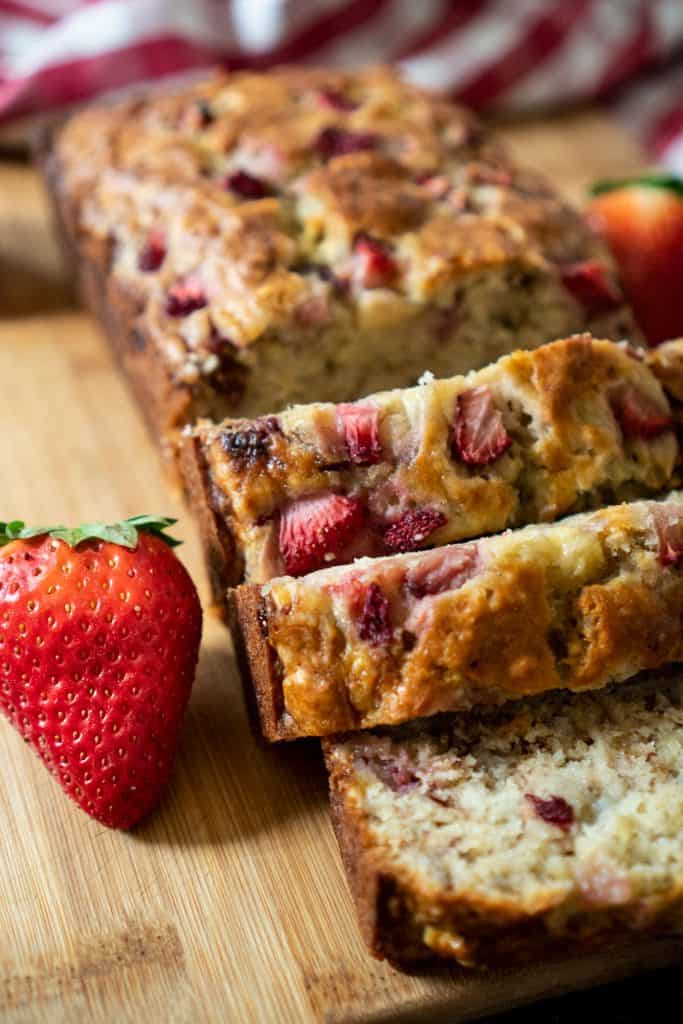 A loaf of strawberry banana bread sliced on a cutting board with strawberries next to it