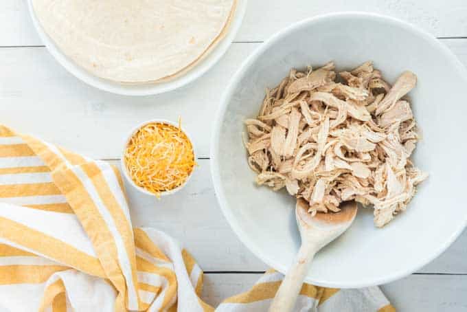 shredded chicken in bowl with cheese and tortillas for enchiladas