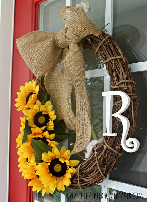 A close up of a grapevine wreath with fake sunflowers, the letter "R" and burlap on a red door