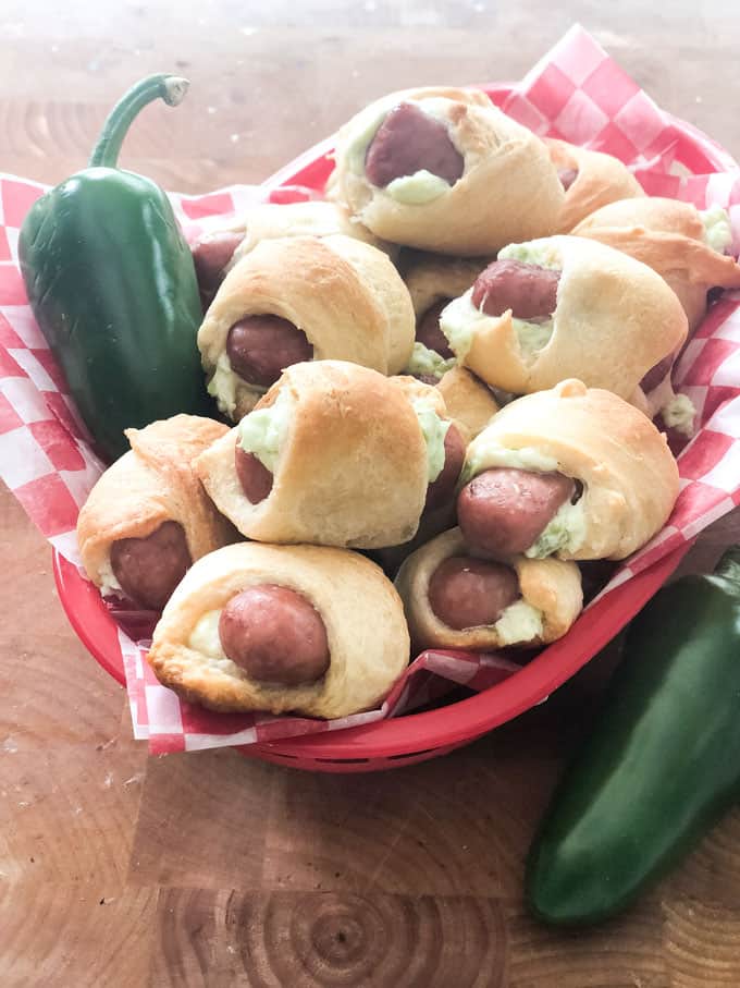 Jalapeño Popper Pigs in a Blanket in a gingham paper lined red basket with whole jalapeños