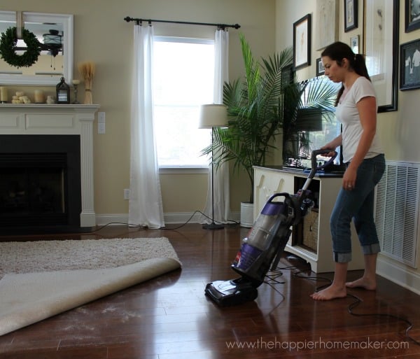 A woman vacuuming underneath of a rug