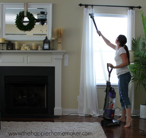 A woman cleaning white curtains in a living room