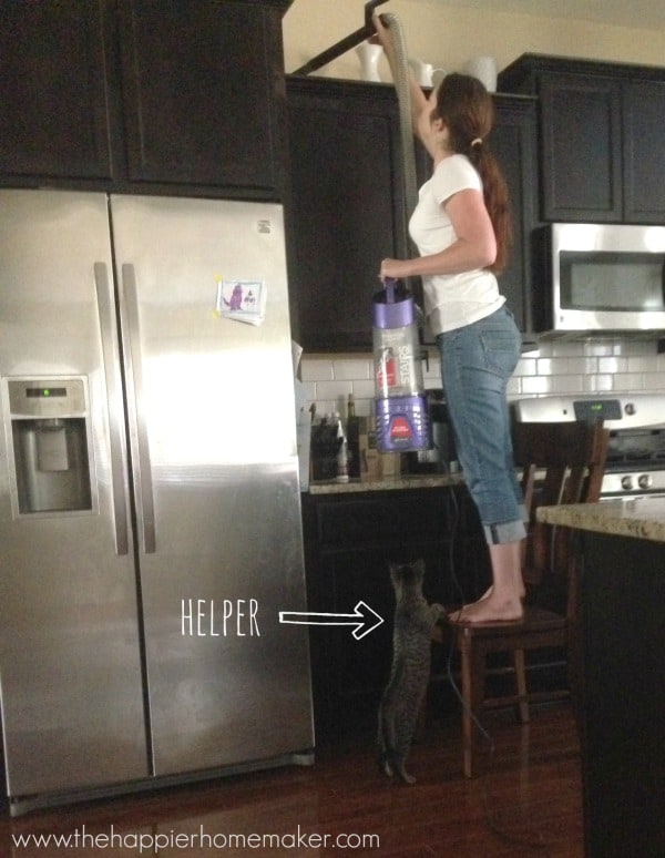 A woman cleaning kitchen cabinets while standing on a chair