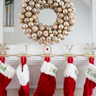 An ornament wreath hanging over a mantel with red Christmas stockings