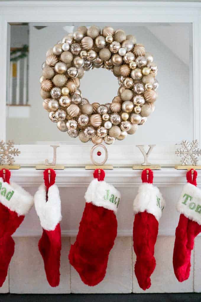 An ornament wreath hanging over a mantel with red Christmas stockings 