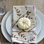 A white plate setting with Autumn napkin with a small white pumpkin on it
