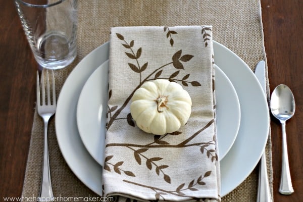 A white plate setting with Autumn napkin with a small white pumpkin on it