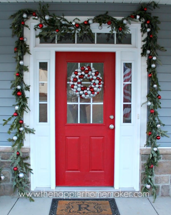 A red front door adorned with Christmas garland made from pine trees