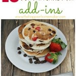 A stack of pancakes with chocolate and strawberries on a white plate and garnished with fresh strawberries and chocolate chips