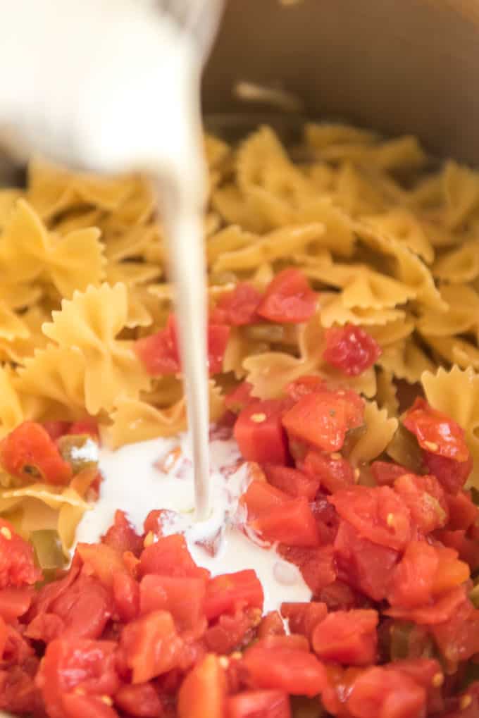cream pouring into pan with raw pasta and diced tomatoes