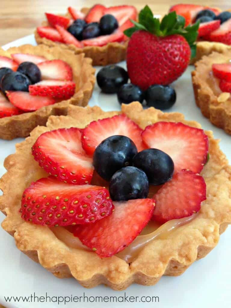 A close up of berry tarts topped with sliced strawberries and blueberries