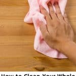 A hand wiping down a table with a pink cleaning cloth