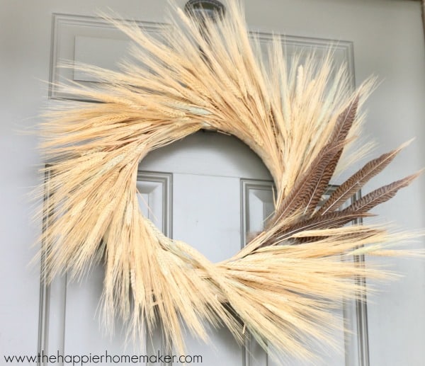 A close up of a wheat autumn door wreath with feathers