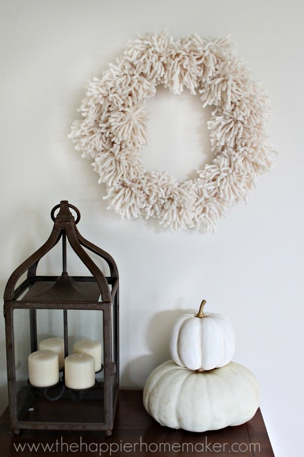 A DIY giant pompom wreath hanging over a white pumpkin and lantern