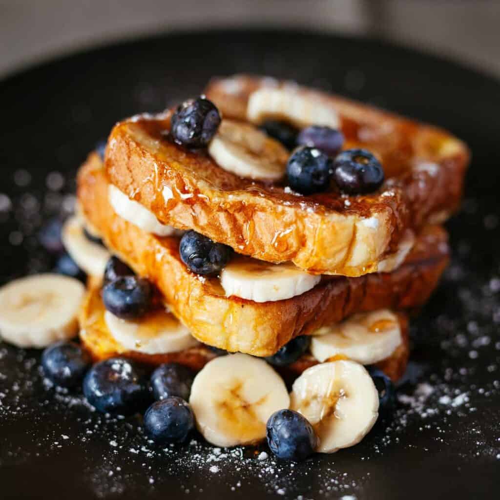 french toast with bananas and blueberries on dark plate