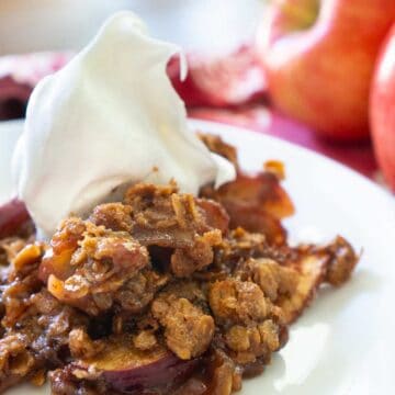 peanut butter apple crisp on white plate with whipped cream on top