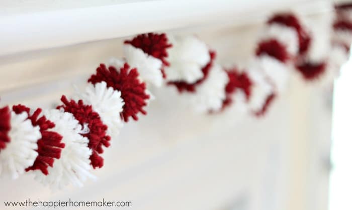 A close up of Valentine\'s Day mini pom pom garland hanging on a white mantel 