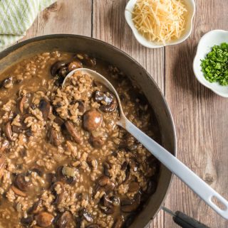 mushroom risotto in bowl with spoon and parmesan cheese and herbs