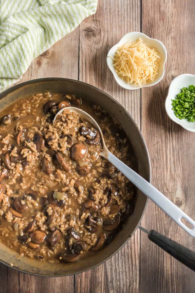 mushroom risotto in bowl with spoon and parmesan cheese and herbs