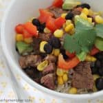 A close up of a bowl of a burrito bowl topped with cilantro, corn and red peppers
