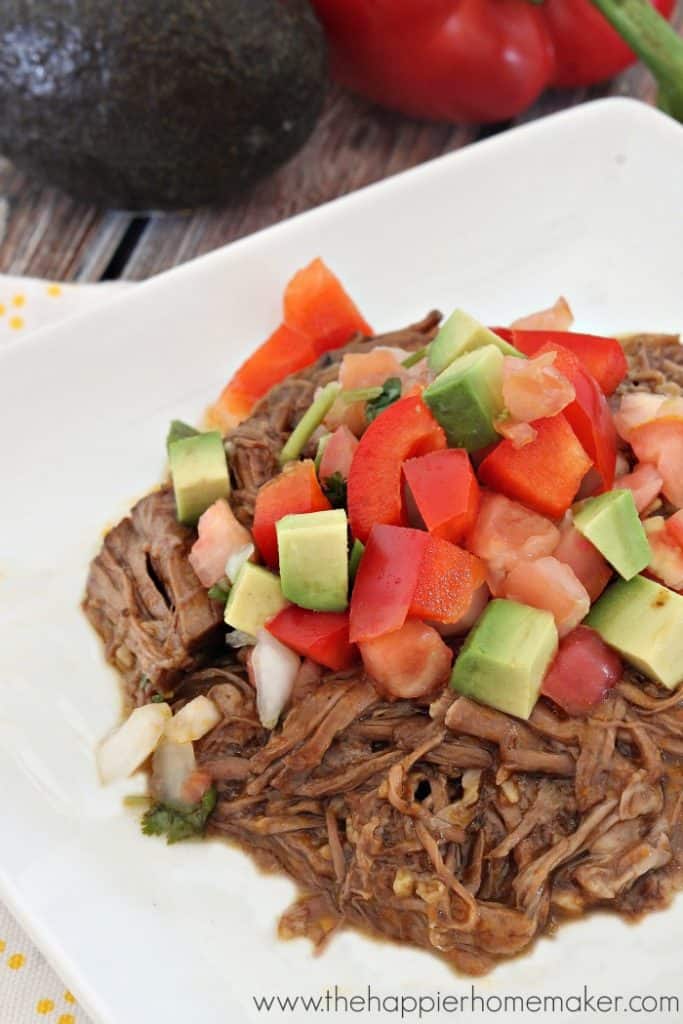 A close up of shredded beef topped with red peppers and avocado 
