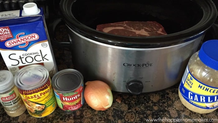 A slow cooker with an onion and other ingredients next to it