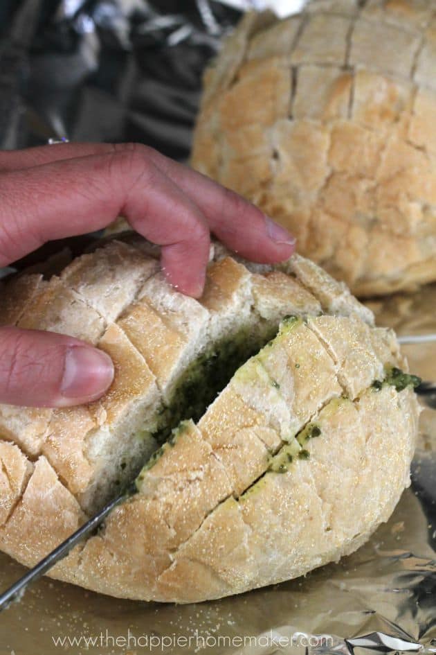 An in-process picture of someone making pesto cheesy pull apart bread by putting pesto in-between the pieces that have been cut