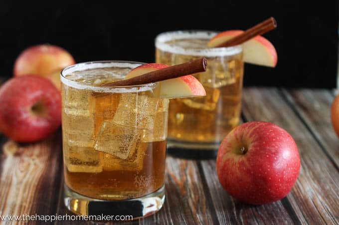 Two glasses of apple cider ginger beer garnished with a cinnamon stick and a apple slice