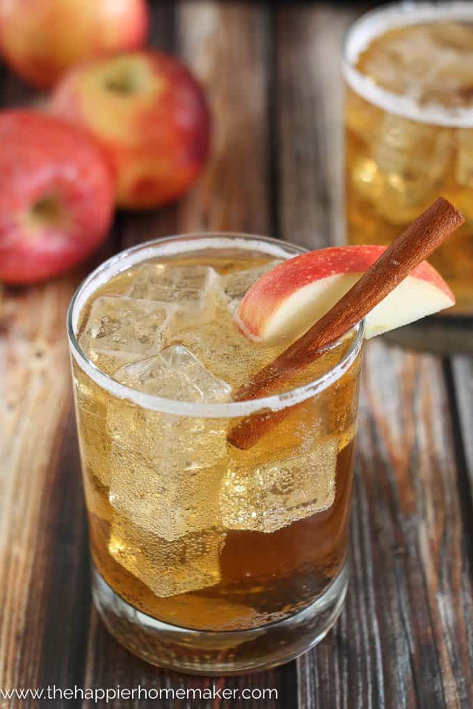 A close up of a apple cider ginger beer cocktail garnished with a slice of apple and a cinnamon stick