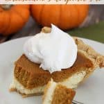 A piece of pumpkin pie cheesecake topped with whipped cream and two orange pumpkins in the background