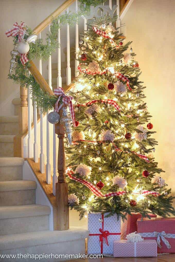 A brightly lit and decorated Christmas tree next to a stairwell 