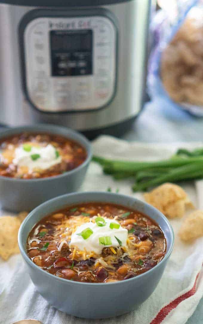 Taco Soup in gray ceramic bowls topped with sour cream and green onion in front of instant pot