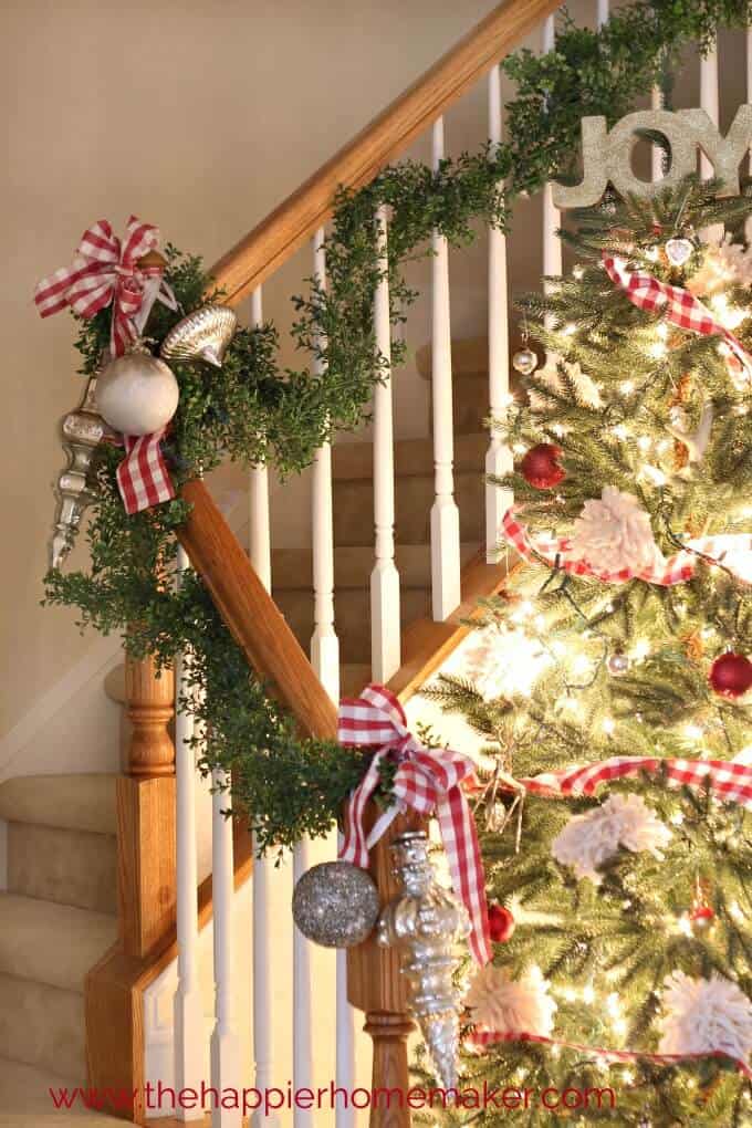 A close up of a Christmas tree, garland going up a staircase and silver ornaments
