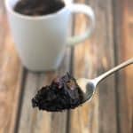 A spoonful of brownie mix in front of a white coffee cup on a wood table