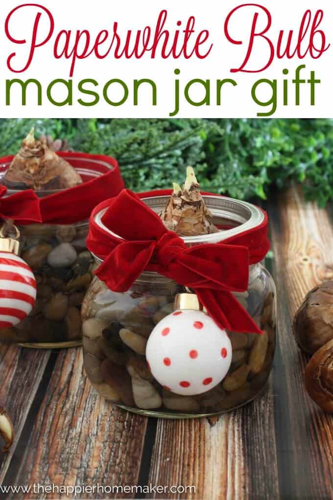 A small mason jar filled with rocks as a paperweight with a velvet red ribbon and a white and red Christmas ornament 