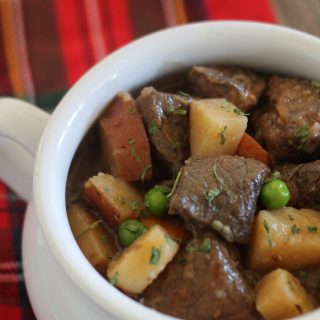 A white bowl of slow cooker beef stew on a plaid napkin