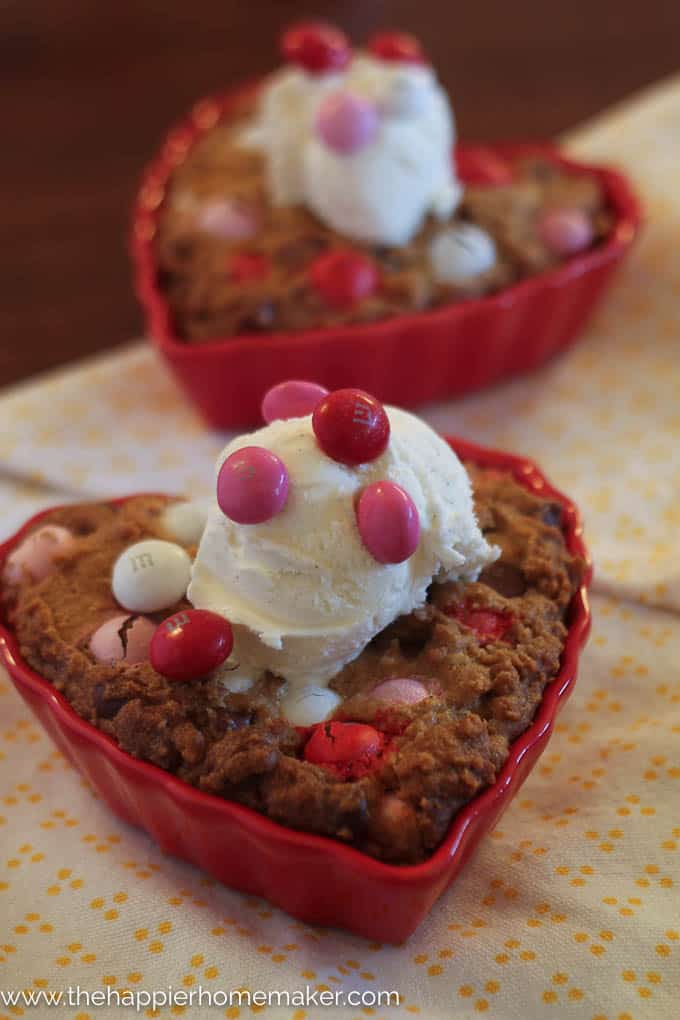 Two peanut butter MM chocolate chip cookies shaped like hearts topped with ice cream and M&Ms