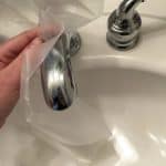 Someone rubbing plastic wrap on a chrome faucet to prevent water stains
