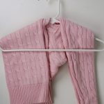 A close up of a pink sweater being hung on a plastic hanger so that the sweater is not stretched